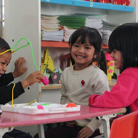 Three Vietnamese schoolchildren sit at a table playing and smiling