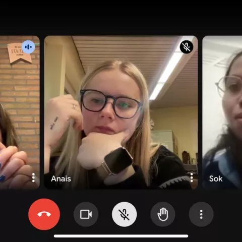 A video call with three people, each in their own video window. The mood appears focused. One person has a background with brick and banners.