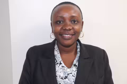 Jemma is in a black blazer and patterned blouse. She is standing against a plain white background.