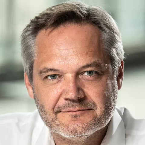 Joris looks at the camera wearing a white shirt. The background is blurred.