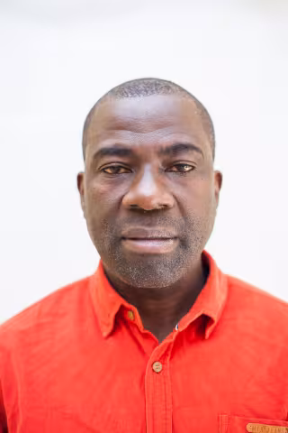 Kennedy is in an orange shirt against a light background, displaying a calm, neutral expression.