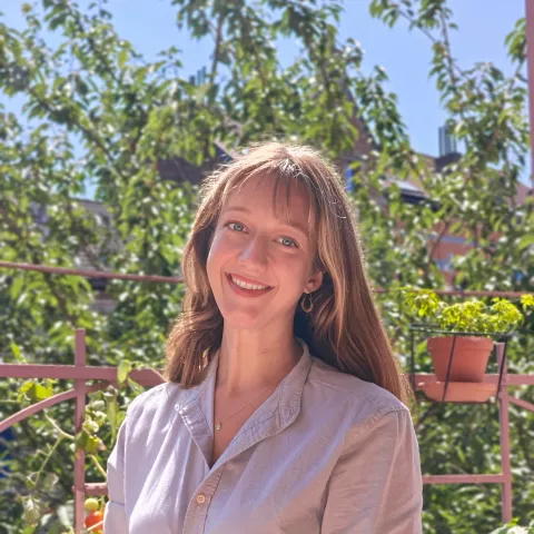 Lara is wearing a light shirt. Greenery in the background suggests a sunny garden setting, conveying warmth and cheerfulness.