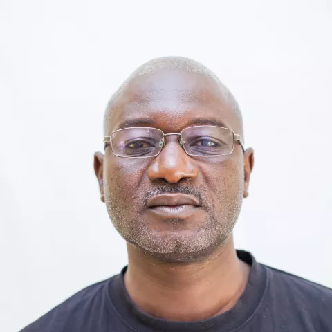 Lyson is wearing a black T-shirt, standing against a plain white background. 
