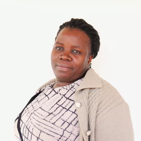Margaret smiles softly, wearing a patterned blouse and a beige cardigan. The background is plain white.