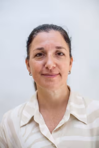 Miranda is wearing a striped white and beige shirt. She smiles against a white background.