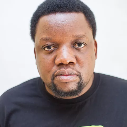 Mwimbu is wearing a black shirt that says "MAKE." The background is plain white.