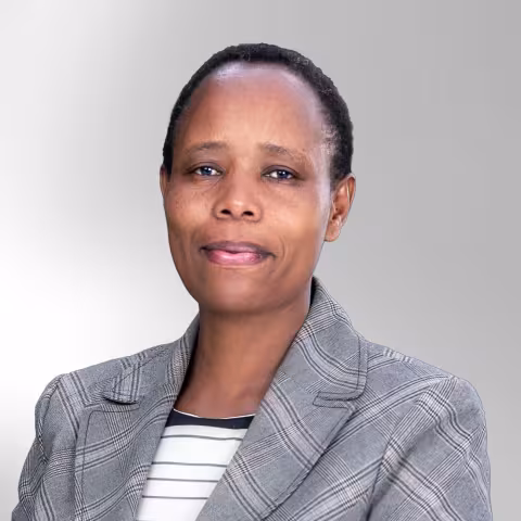 Peninah is wearing a gray plaid blazer and striped shirt smiles subtly against a light gray background.