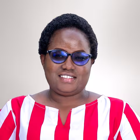 Risper is smiling while wearing blue glasses and a red and white striped shirt against a light gray background.