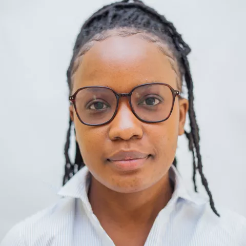 Saliya is wearing brown glasses and smiles lightly. She wears a white shirt against a plain white background.