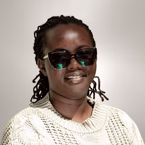 Vane is wearing sunglasses and a knitted sweater. She stands against a plain background. 
