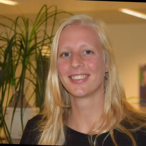 Sofie is wearing a black shirt and smiling. In the background there are plants.