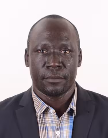 Male staff wearing a dark blazer over a plaid button‑up shirt, photographed against a plain white background.