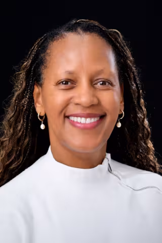 Kevina is smiling at the camera. She has long brained hair and is wearing a white shirt.